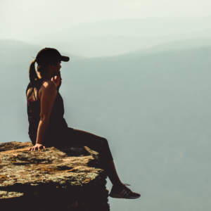 Frau die auf einem Stein sitzt und in die Ferne schaut.